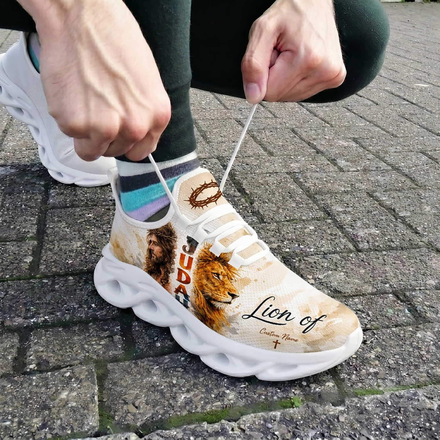 Close-up of a person tying white laces on the custom Jesus and Lion of Judah shoes outdoors on brick pavement