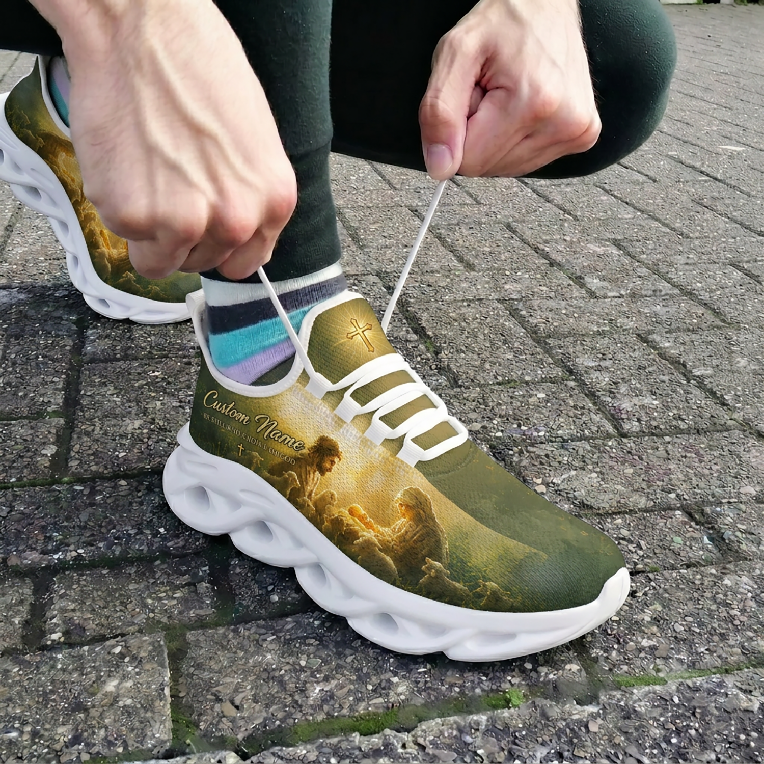 Close-up view of a person lacing up the white custom Nativity scene faith sneakers outdoors on brick pavement