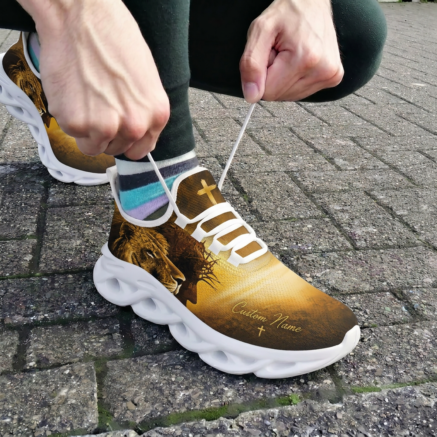 Close-up of a person tying white laces on the custom Jesus and Lion of Judah shoes outdoors on stone pavement