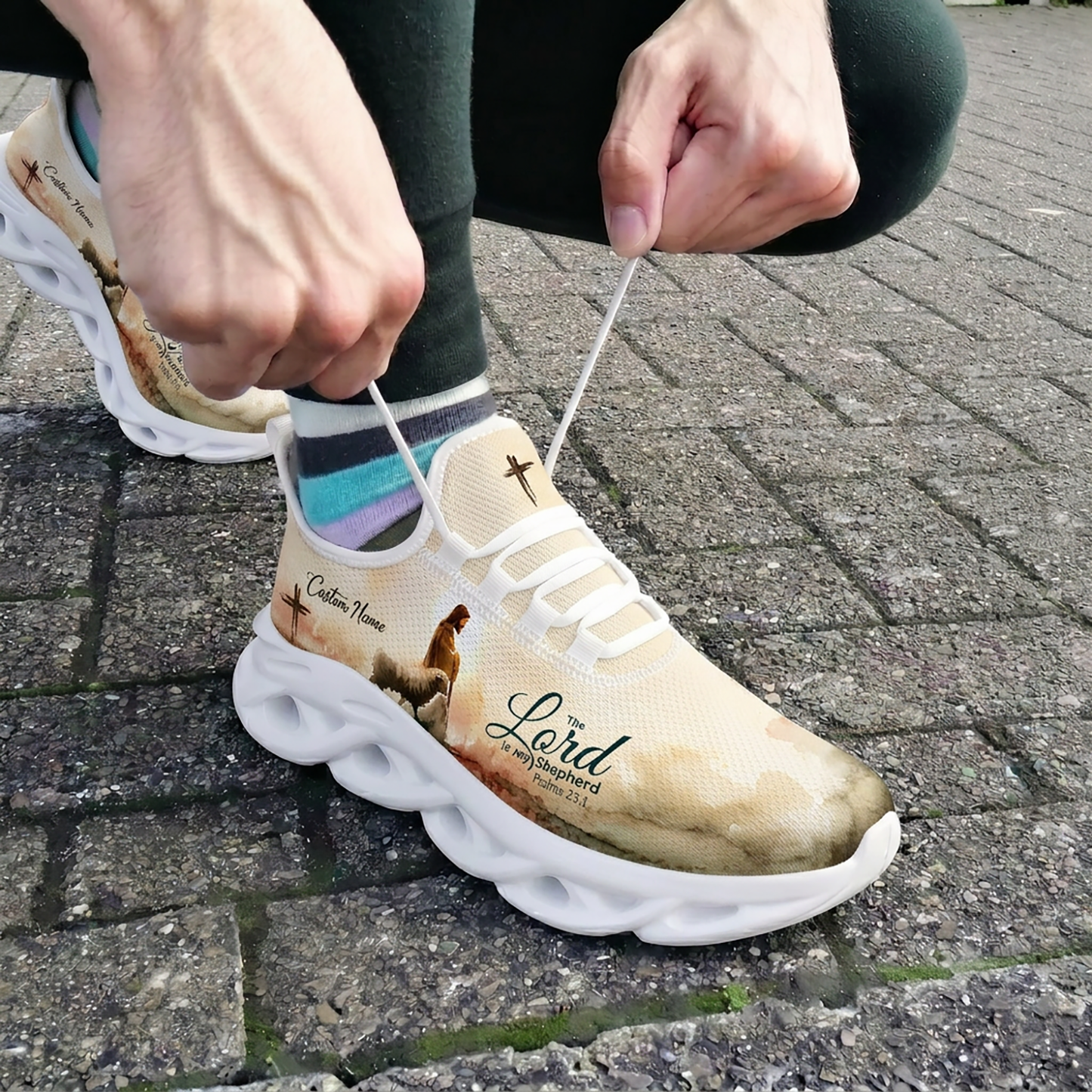 Close-up of a person tying the laces of the custom Psalms 23:1 faith shoes while wearing them outdoors on stone pavement