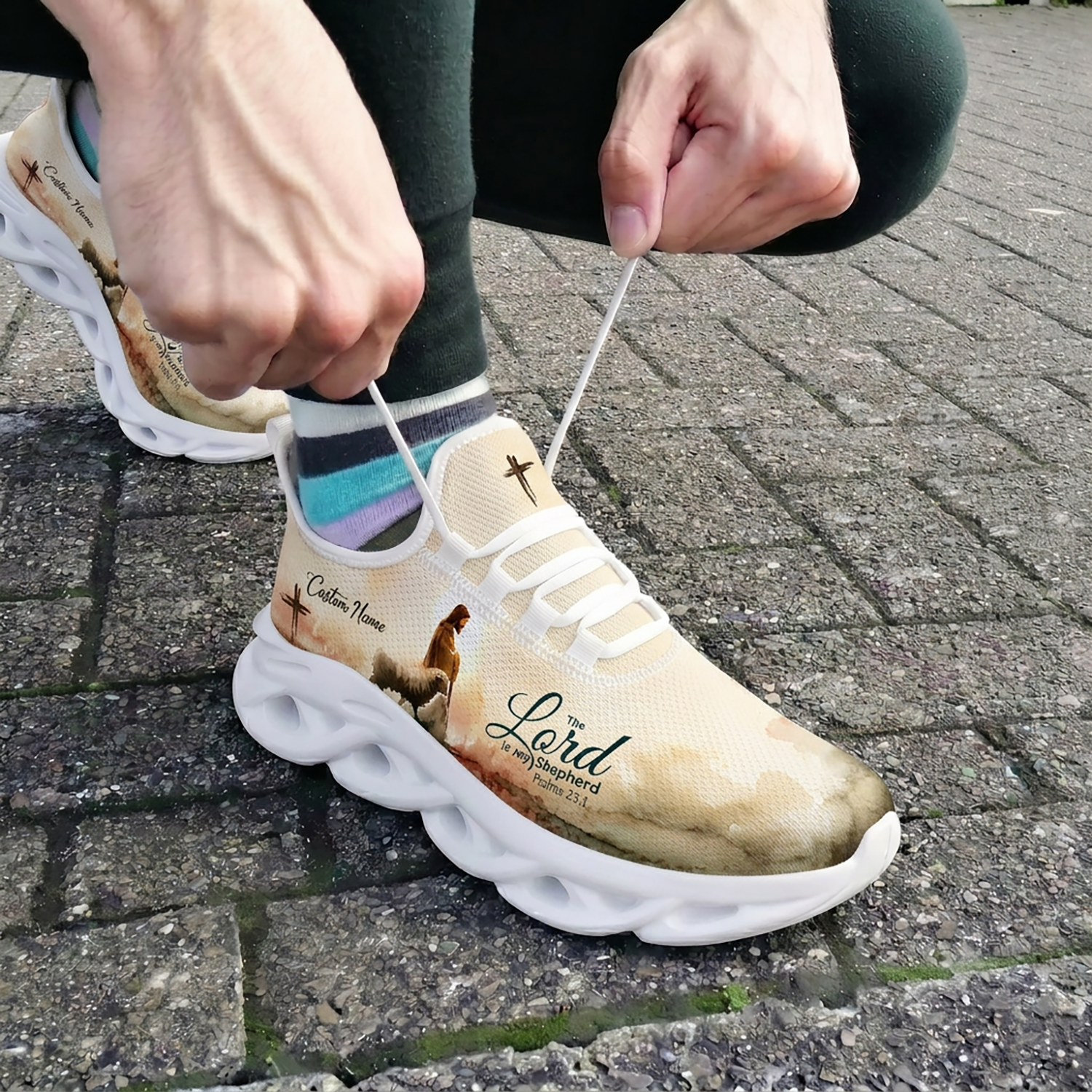 Close-up of a person tying the laces of the custom Psalms 23:1 faith shoes while wearing them outdoors on stone pavement