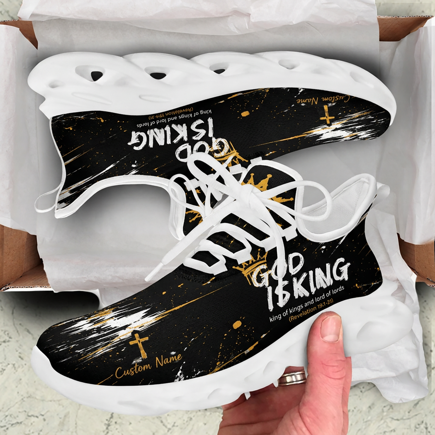 Unboxing display of the Christian black and gold sneakers inside a shipping box, highlighting the Revelation scripture text