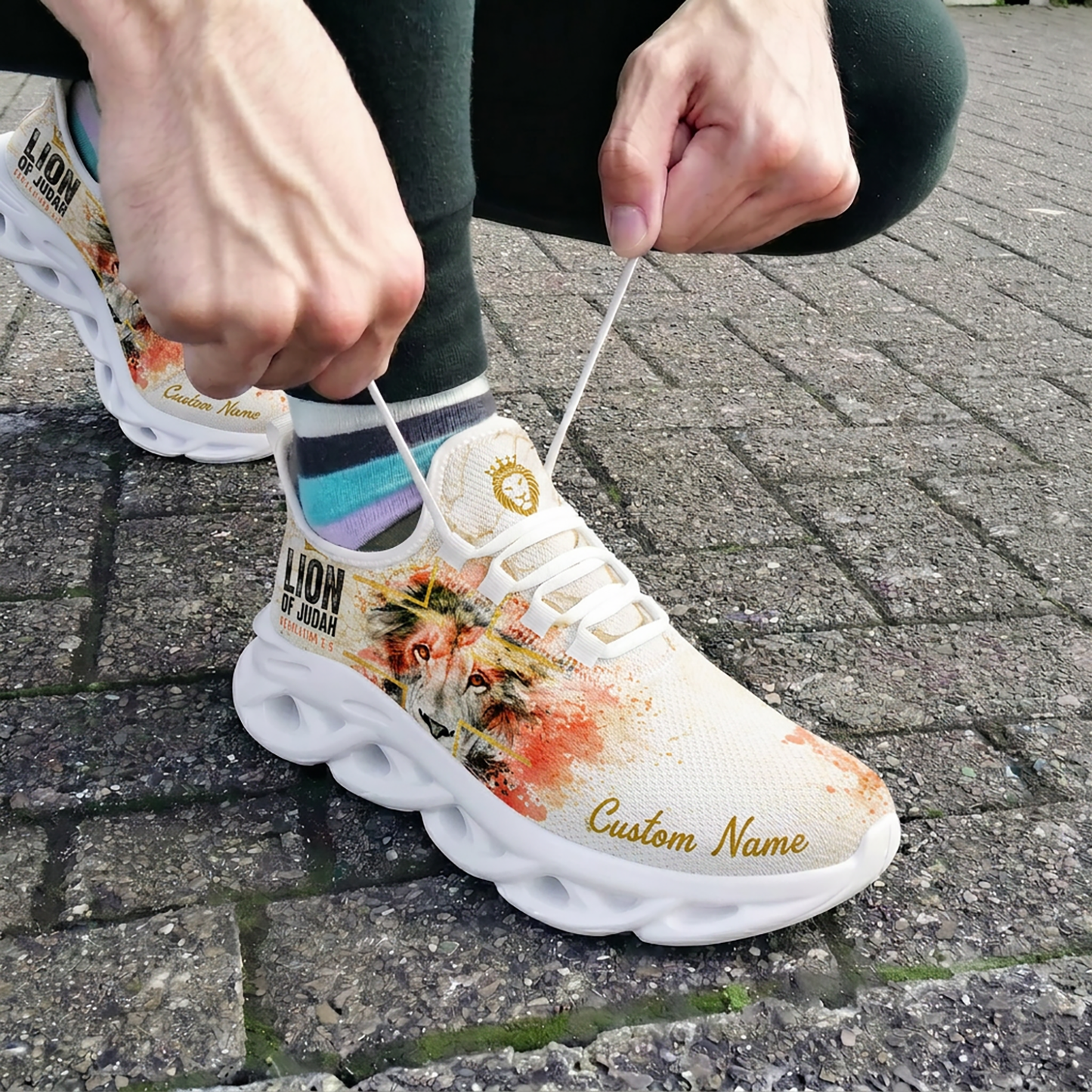 Close-up view of a person tying the laces of the white and orange-red paint splatter Christian shoes on outdoor brick pavement