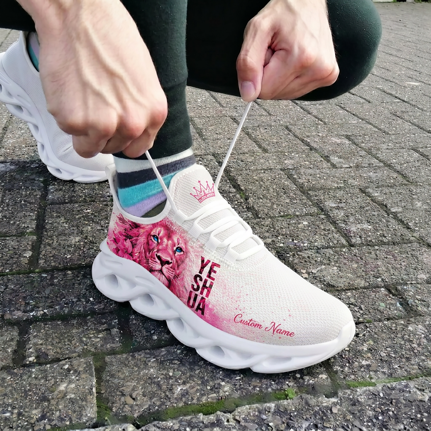 Close-up of a person tying the laces of the custom pink Yeshua faith shoes while wearing them outdoors on stone pavement